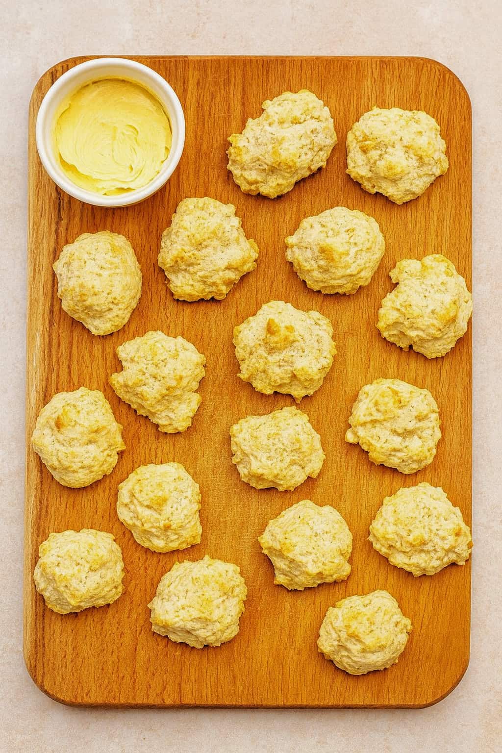 A wooden cutting board with biscuits and a bowl of butter.