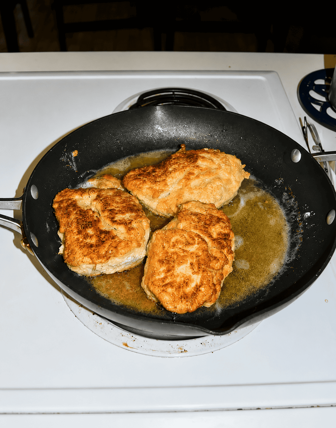 A skillet with three chicken breasts being pan fried.
