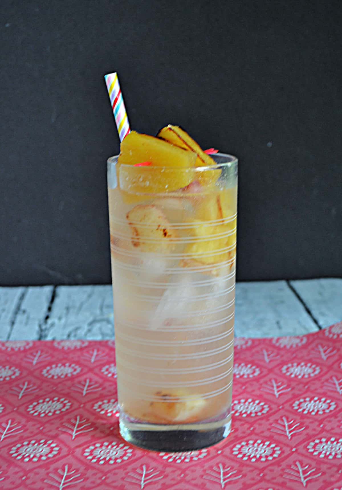 A glass of sangria with grilled pineapple and peaches in it. 