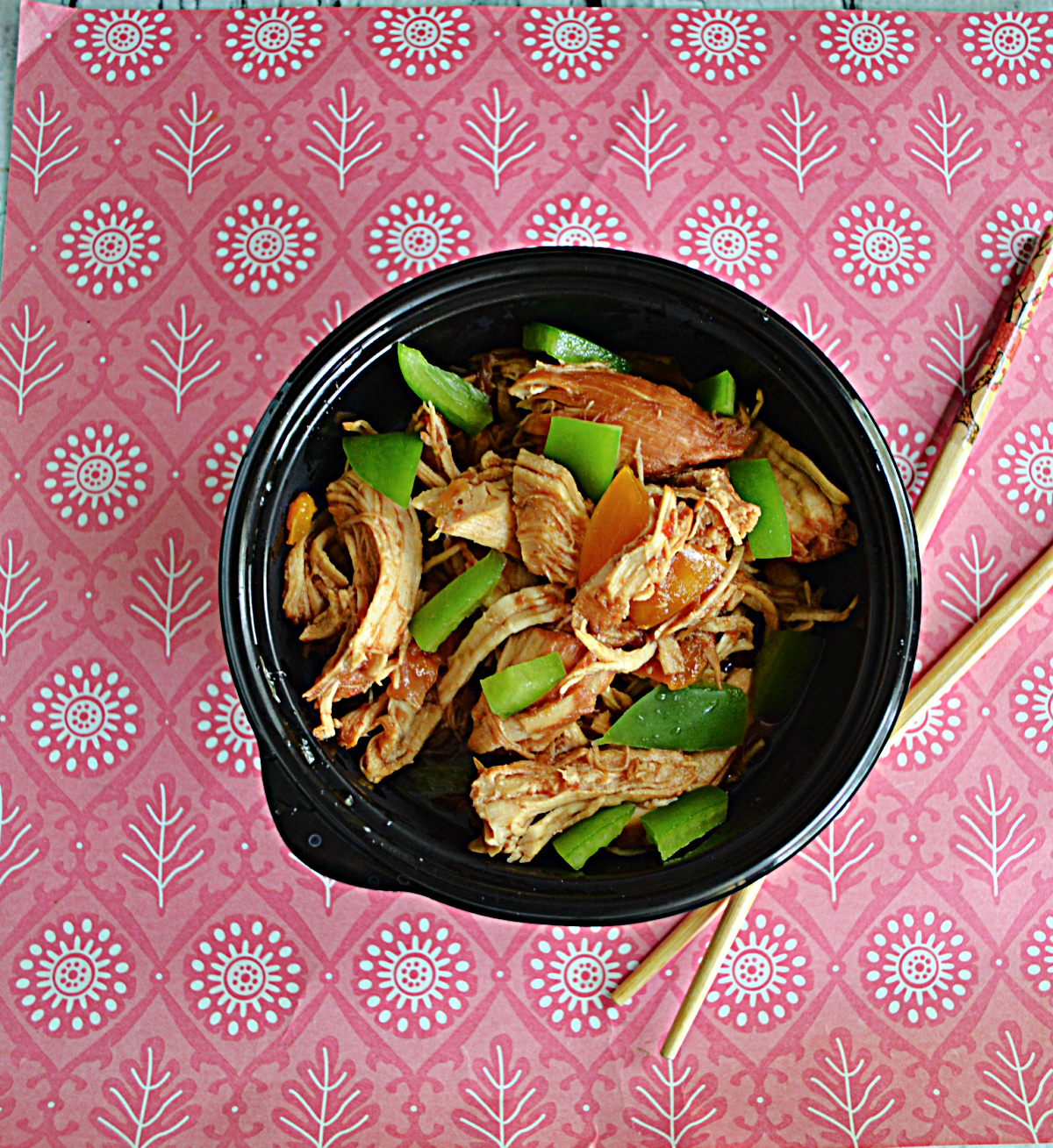 A bowl filled with chicken and green peppers with chopsticks next to the bowl.