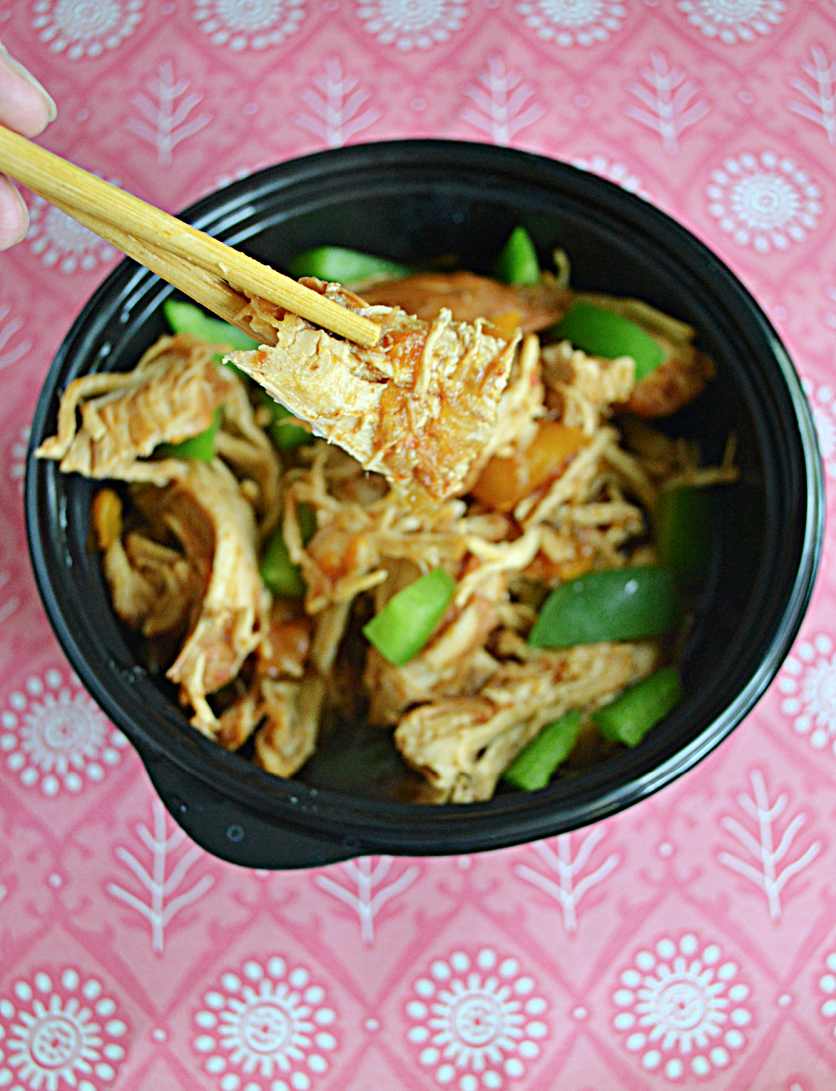 A close up view of bourbon chicken being held up by chopsticks.