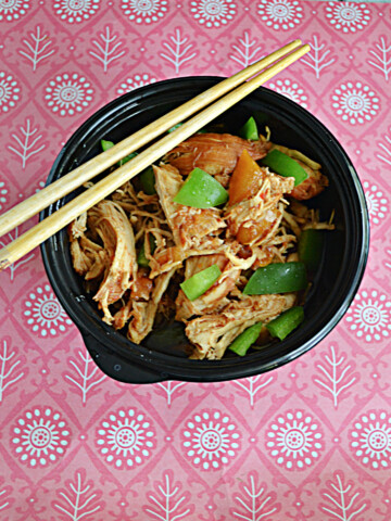 A bowl of bourbon chicken and peppers with chopsticks on the bowl.