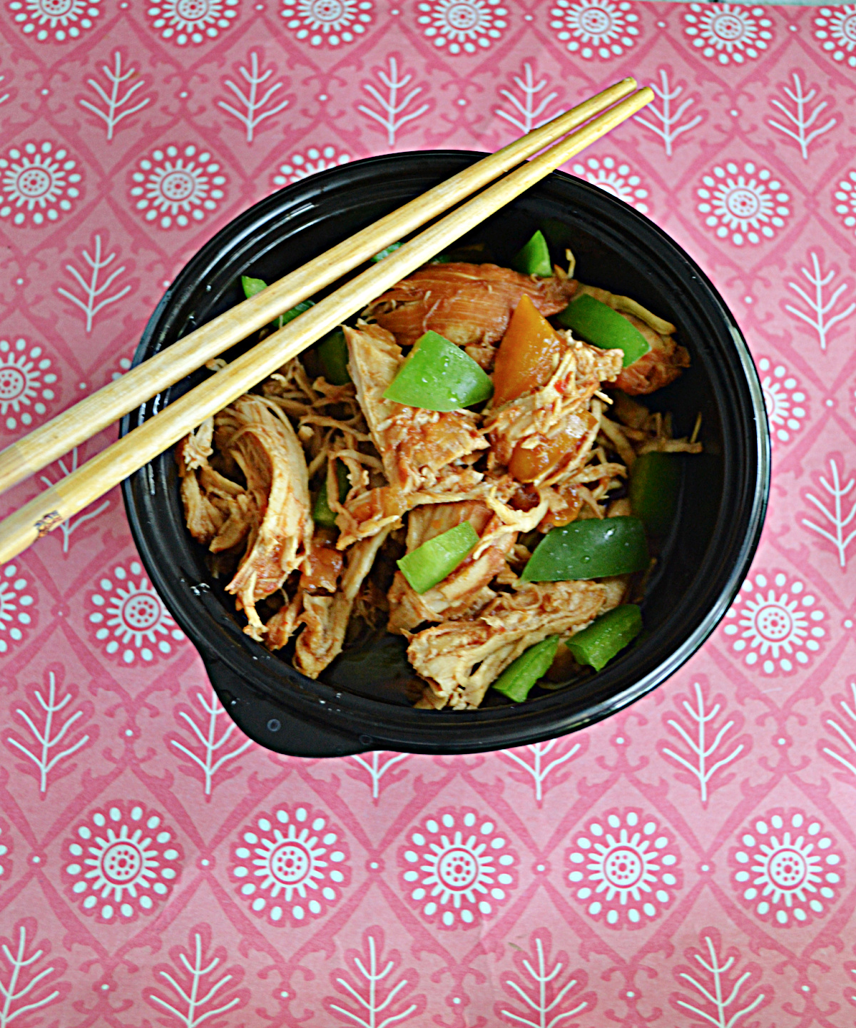A bowl of bourbon chicken and peppers with chopsticks on the bowl. 