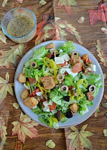 A plate of Italian chopped salad with a bowl of dressing behind it.