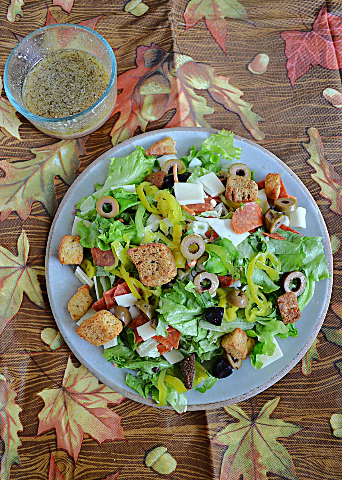 A plate of Italian chopped salad with a bowl of dressing behind it. 