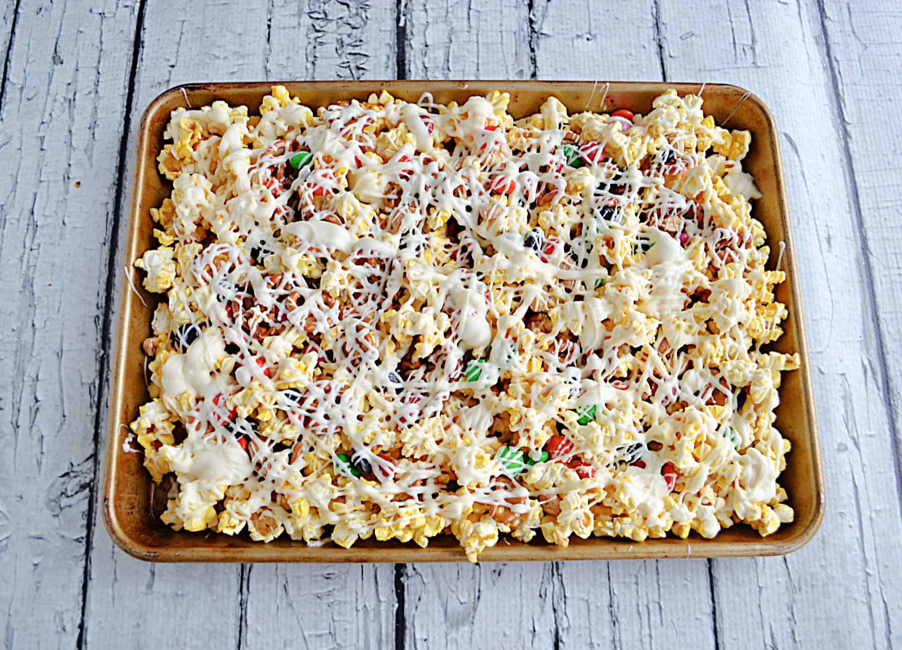 A tray of popcorn, M&M's, and drizzled white chocolate.