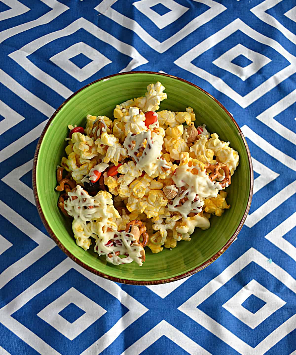 A bowl of popcorn, M&M's, peanuts, and white chocolate drizzle.