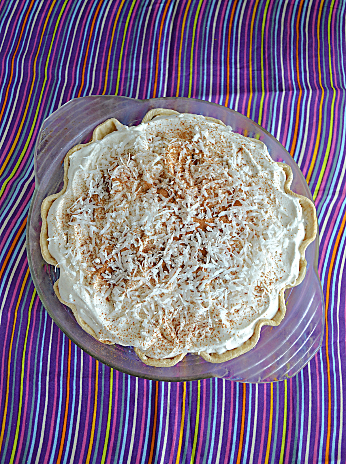 A pie topped with whipped cream, cinnamon, and coconut.