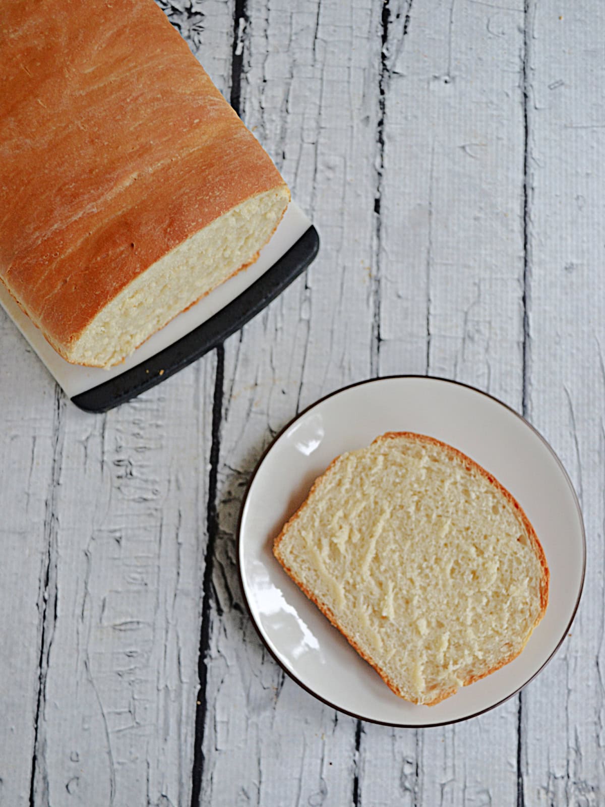 Top view of a plate with a slice of bread on it and a loaf of bread on the side.