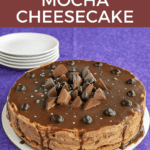 Pin image: Title, a mocha cheesecake with chocolate pieces on top and a stack of plates in the background.