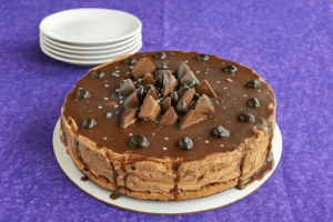 A mocha cheesecake with chocolate pieces on top and a stack of plates in the background.