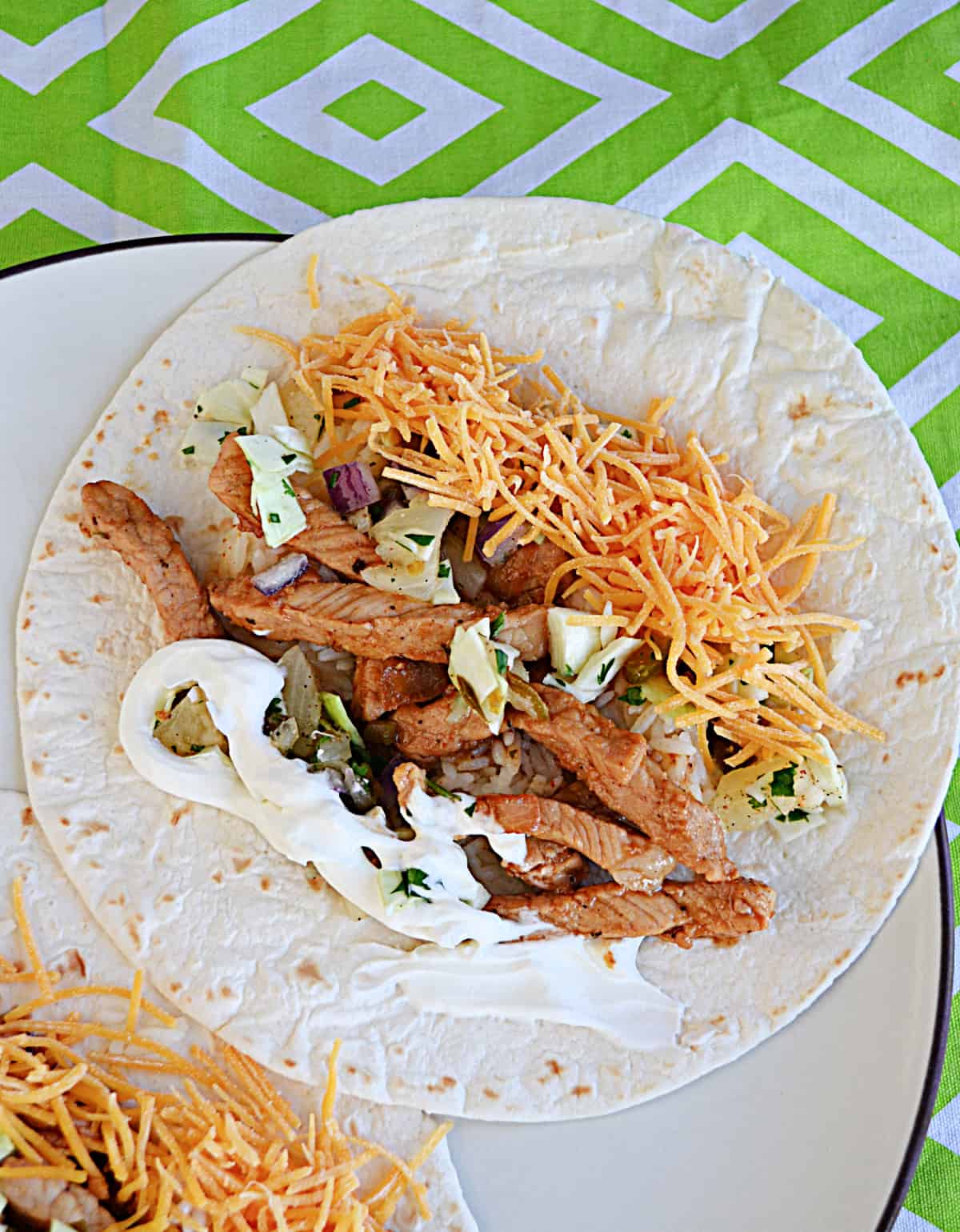 A close up of a pork taco with cheese, sour cream, and slaw. 