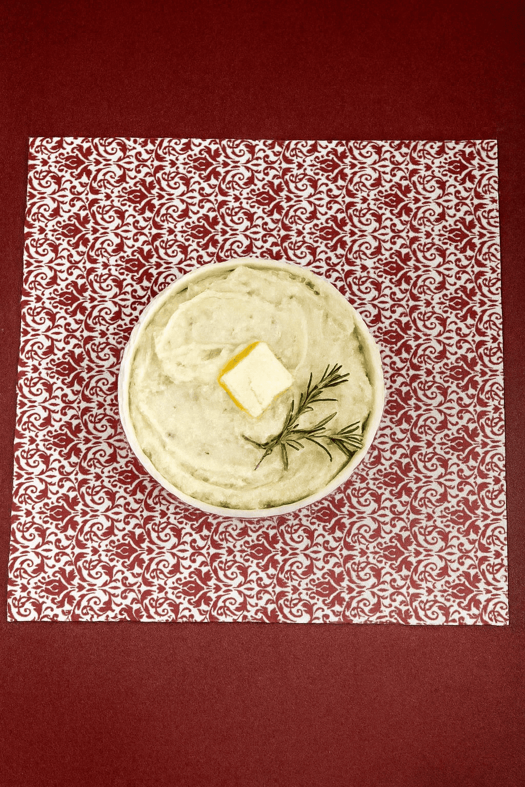 A red background with a bowl of mashed potatoes on top of it.