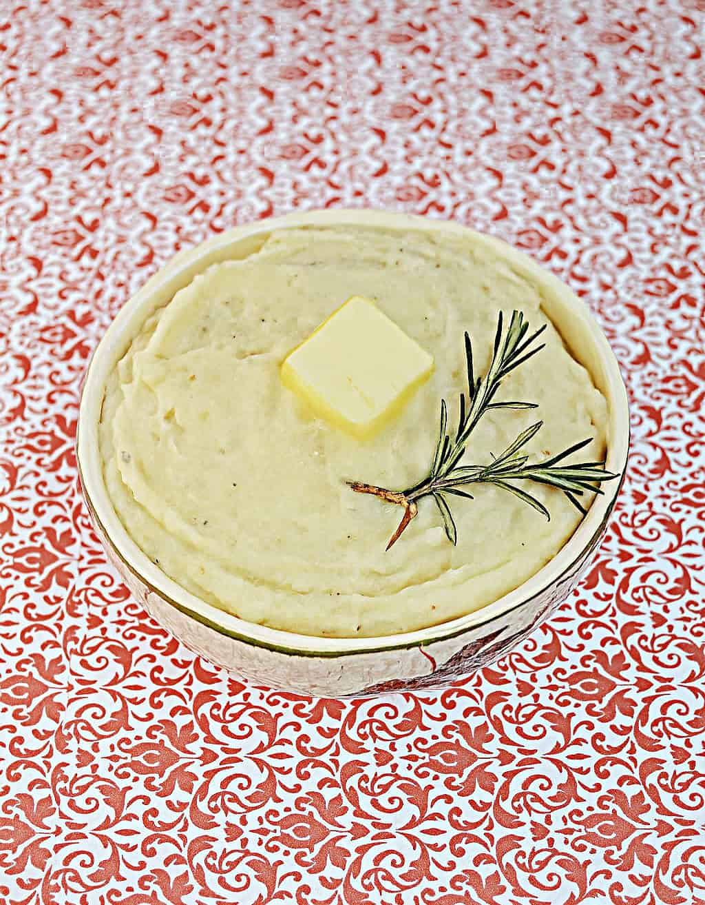 A top view of a bowl of rosemary potatoes with a pat of butter and 2 sprigs of rosemary.