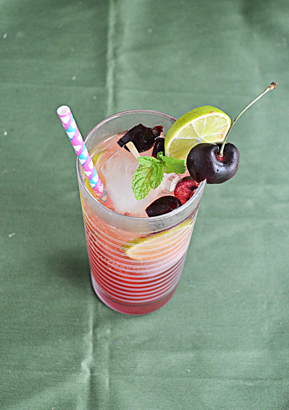 A top view of a glass of cherry mojito with lime, cherries, and mint on top.