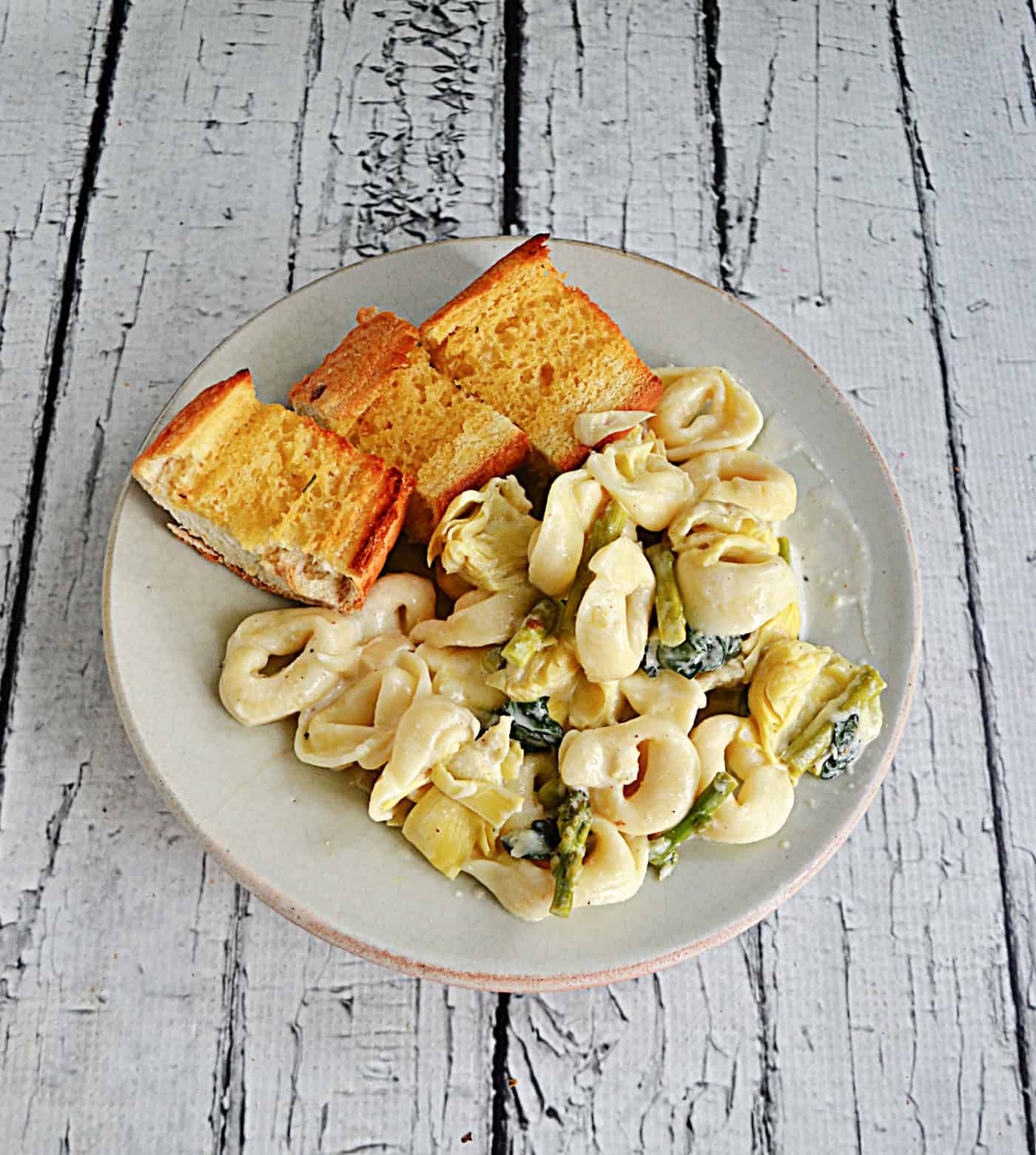 A plate of tortellini with slices of garlic bread.