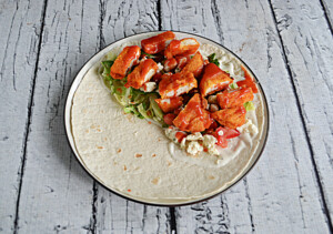 A wrap with lettuce and buffalo chicken on top of it.