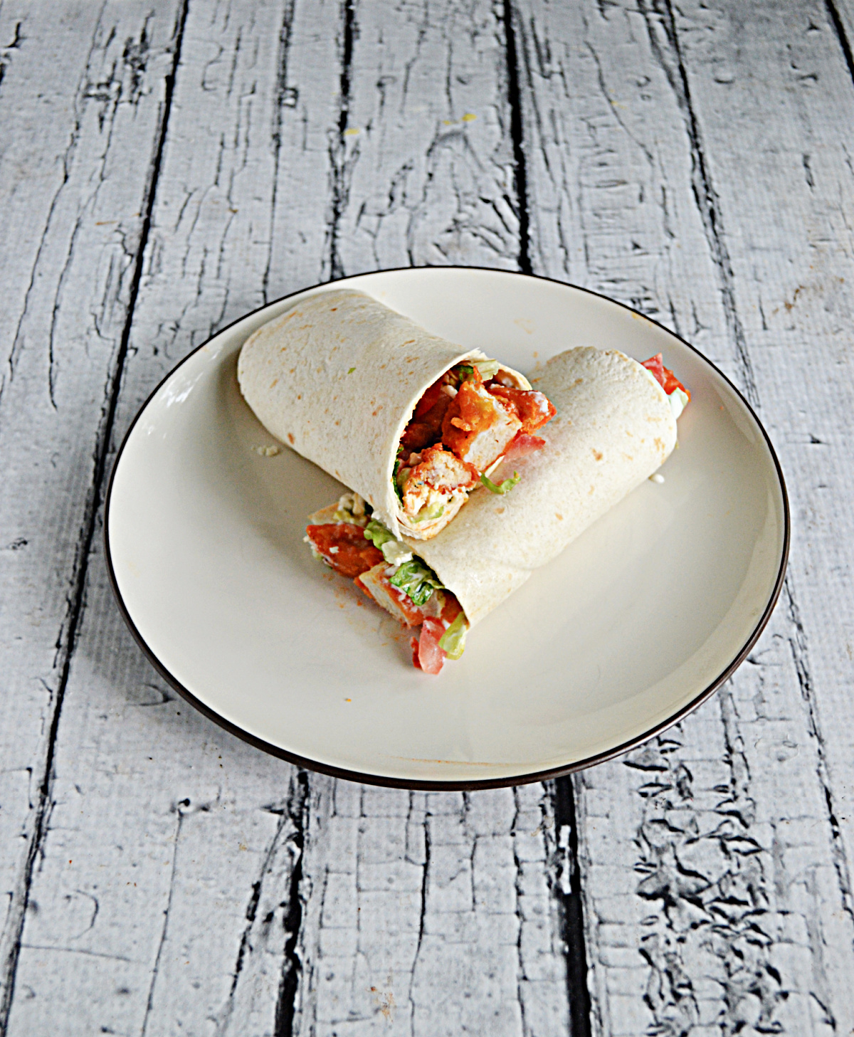 A plate with a buffalo chicken wrap cut in half and stacked on top of each other.