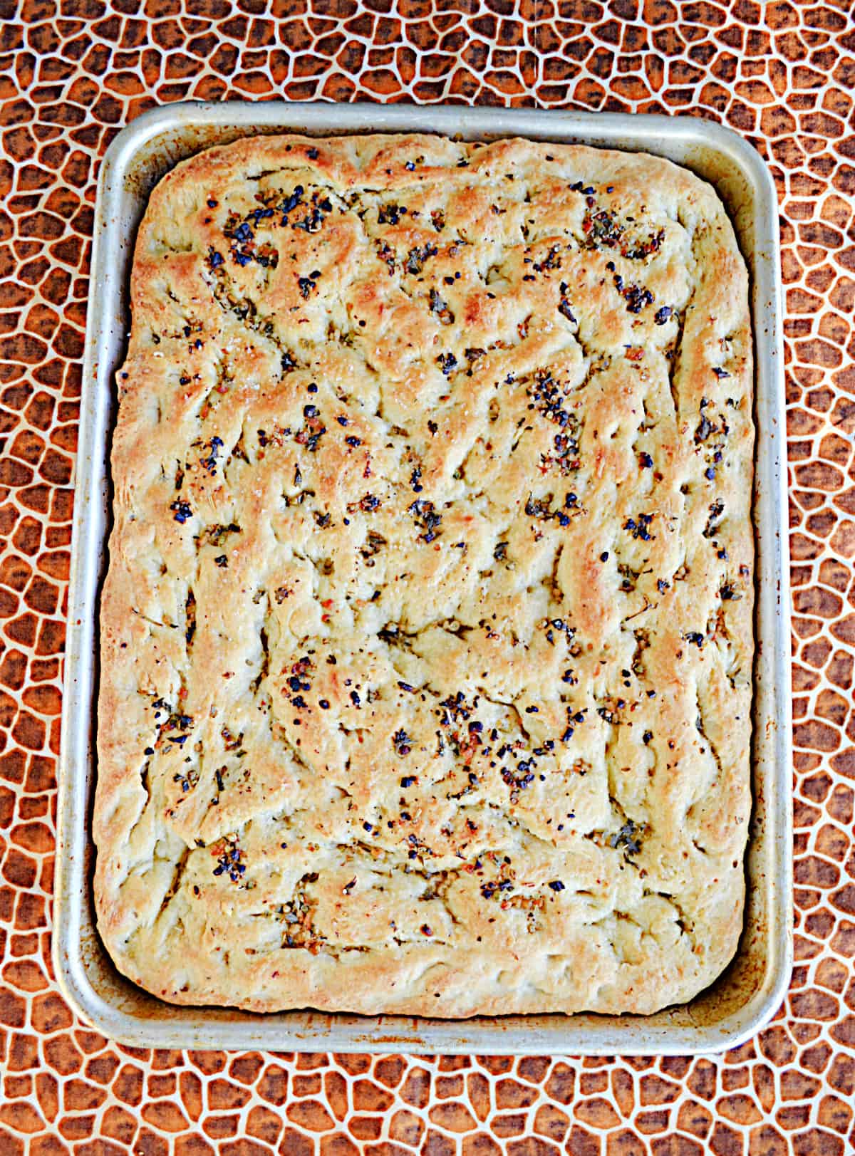 A pan of golden brown focaccia bread with herbs on top. 