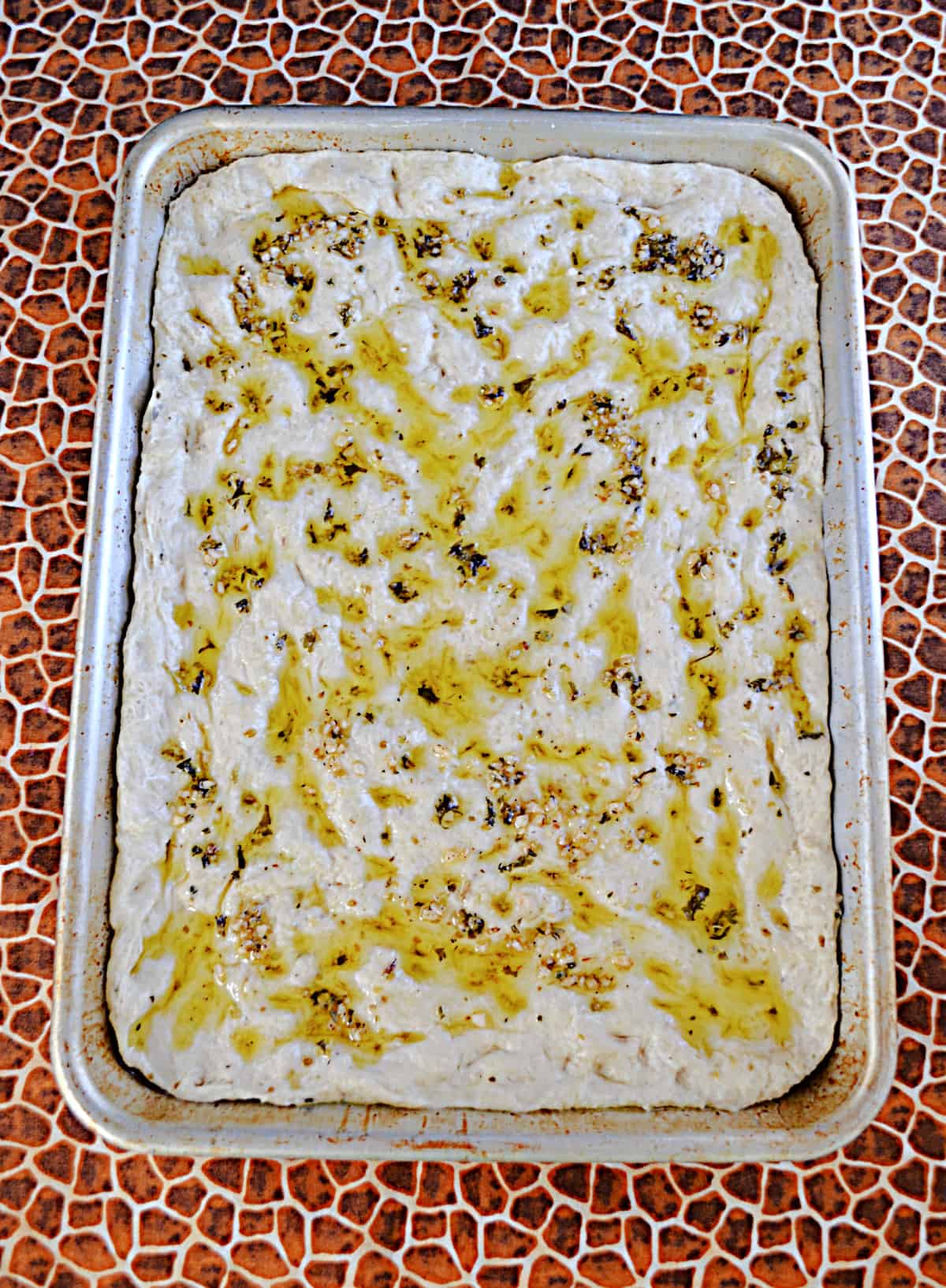 A pan of bread dough with olive oil drizzled over top of the dough.