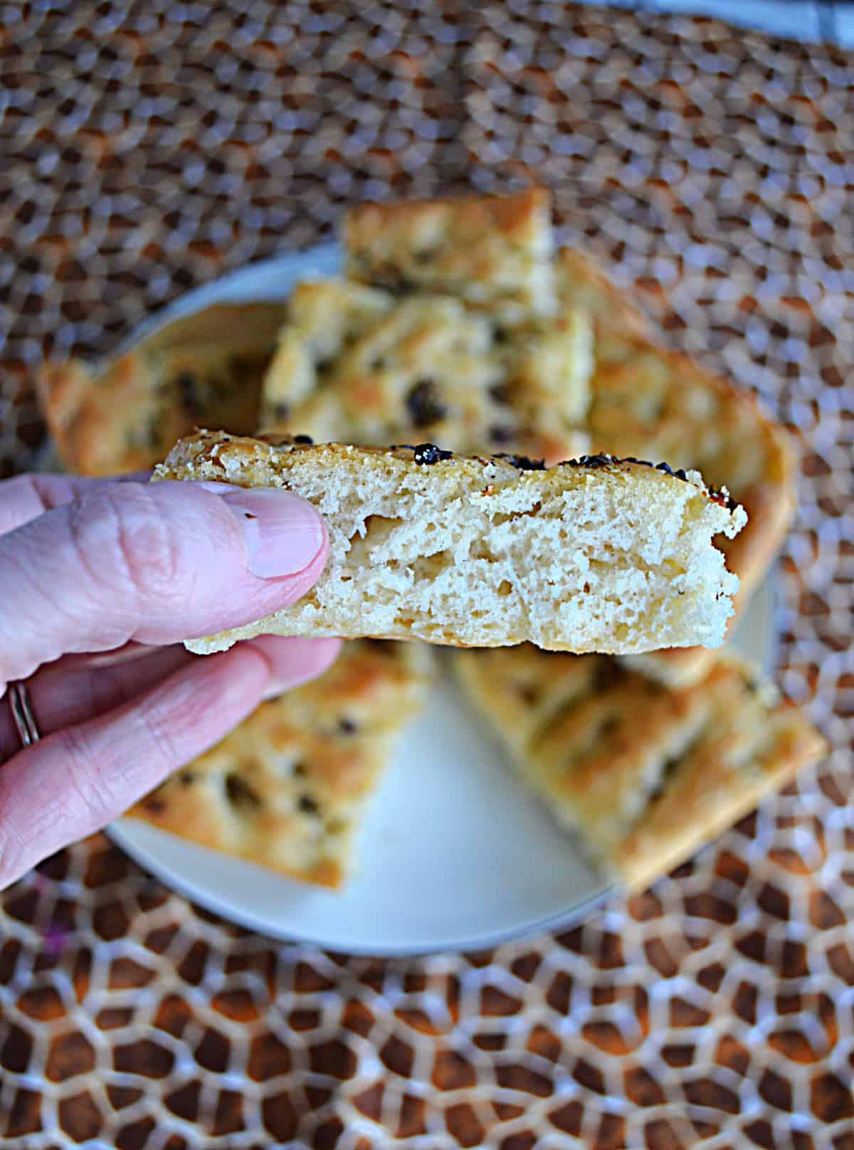 A hand holding a slice of focaccia bread. 