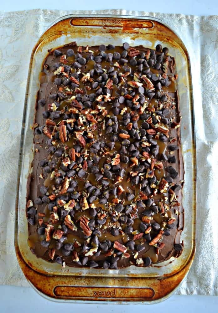 Guests will love to dig into this Chocolate Turtle Poke Cake topped with pecans, caramel, and chocolate chips!