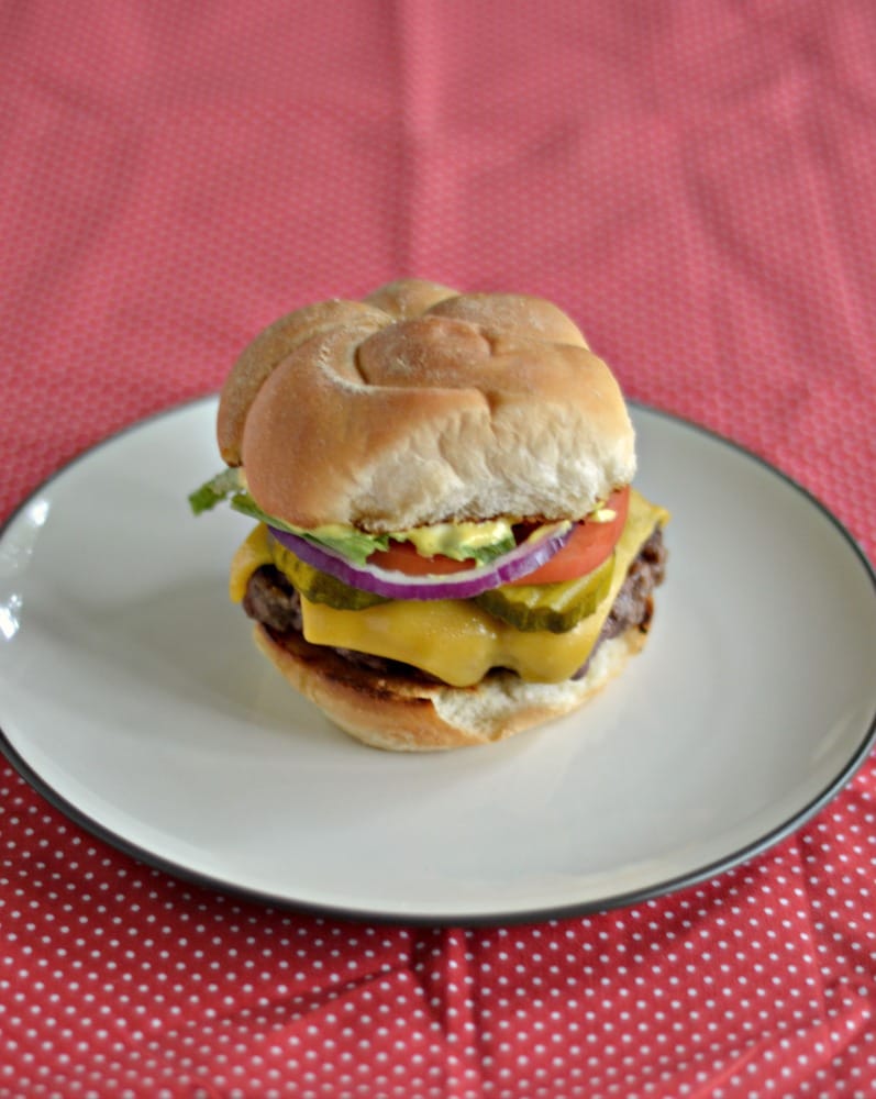 A close up of a burger topped with cheese, pickles, tomato, red onion, and a mustard sauce. 