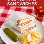 Pin Image: Title, Two wrapped sandwich halves, a handful of chips, and a pickle on a plate with a glass of iced tea behind the plate.