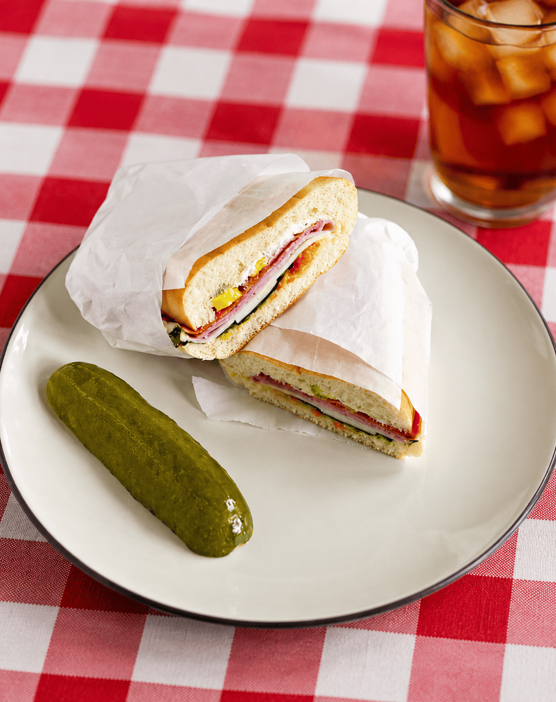 A plate with 2 sandwich halves glass of iced tea behind the plate.