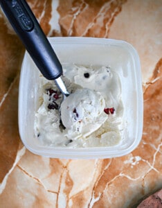 A container of cherry vanilla ice cream with an ice cream scoop in it.