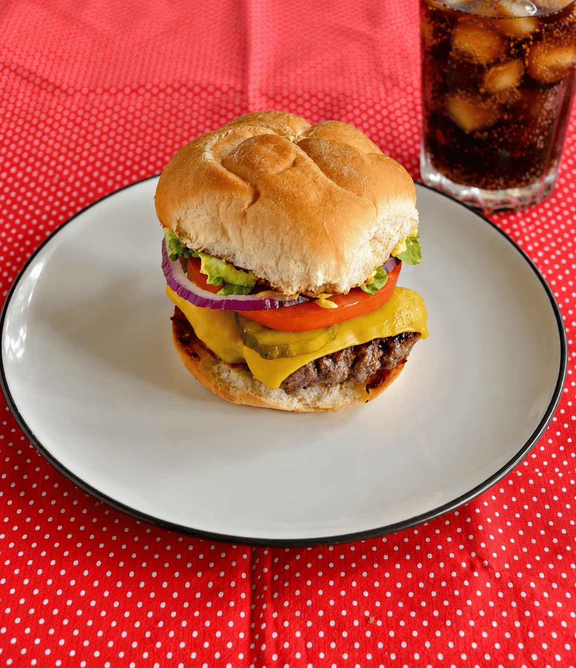 A giant smashburger on a plate with a glass of soda behind it.