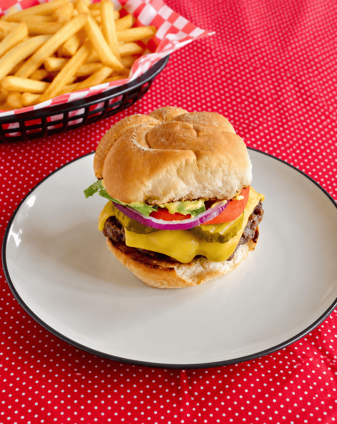 A plate with a smashburger on it with a basket of fries behind the plate.