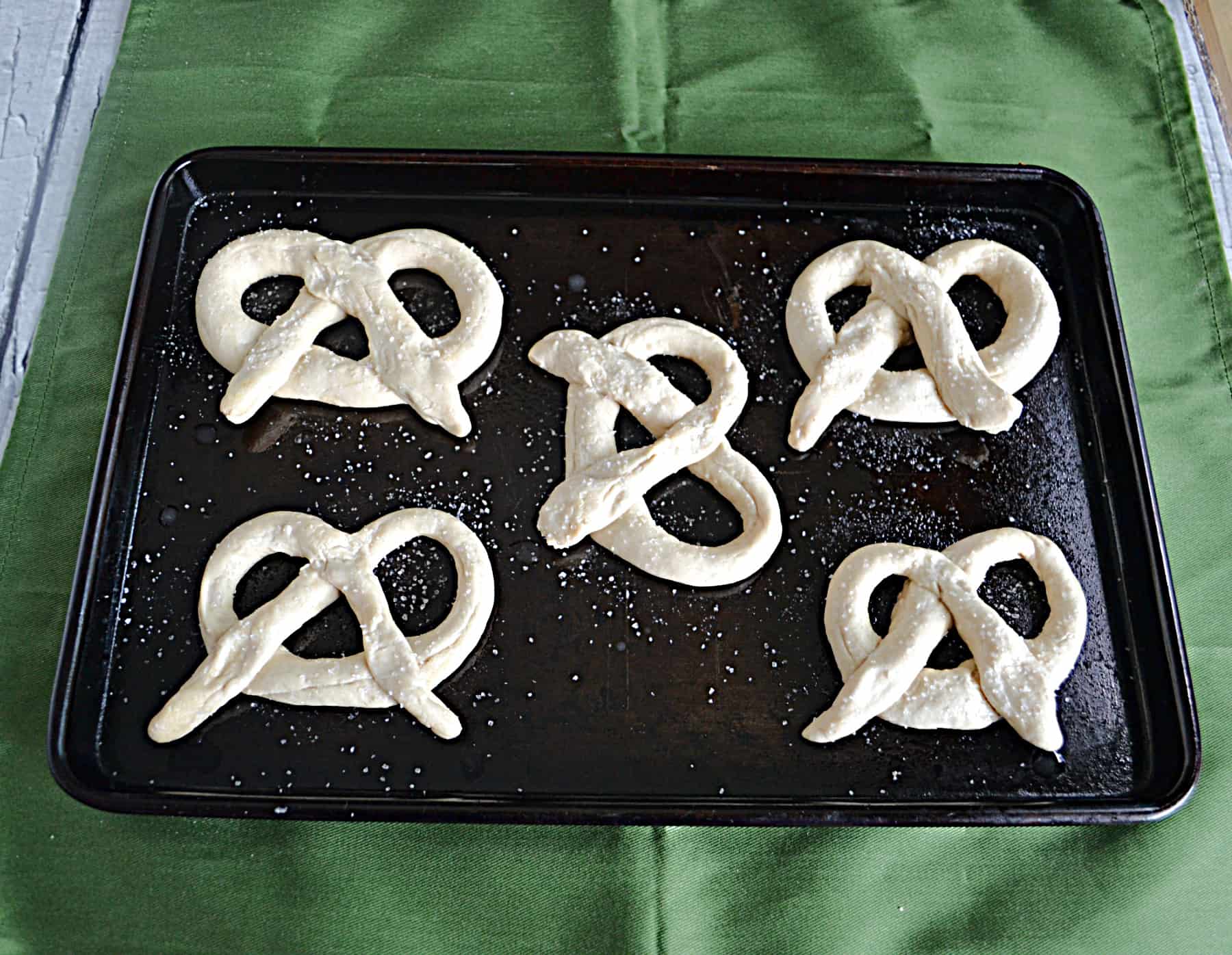 A baking pan with five uncooked pretzels on it.