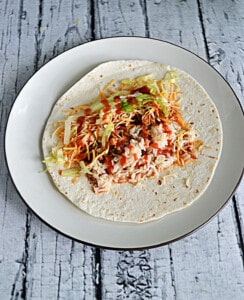 A plate with a tortilla topped with chicken taco ingredients.