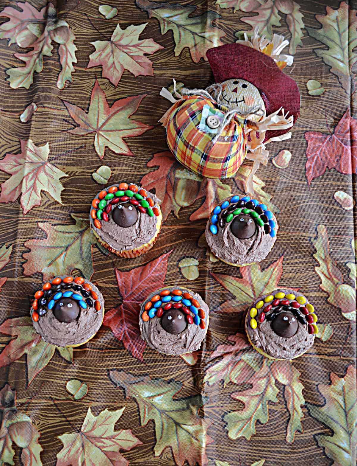 Five turkey cupcakes with a scarecrow behind them.
