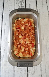 A loaf pan with batter and chopped apples on top.