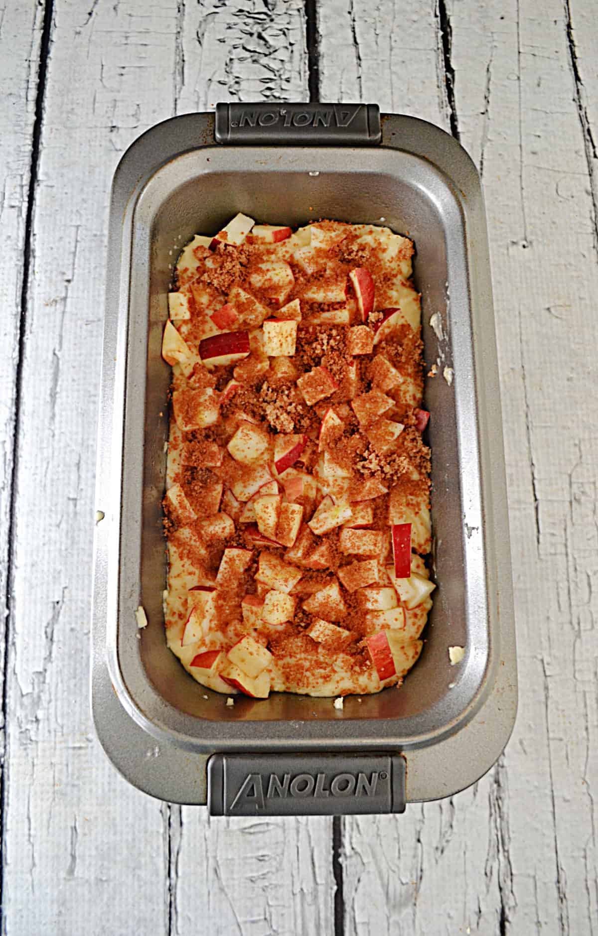 A loaf pan with batter and chopped apples on top.