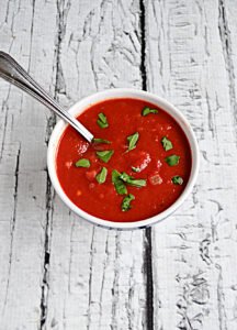 A top view of a bowl of tomato sauce with parsley on top and a spoon in the sauce.