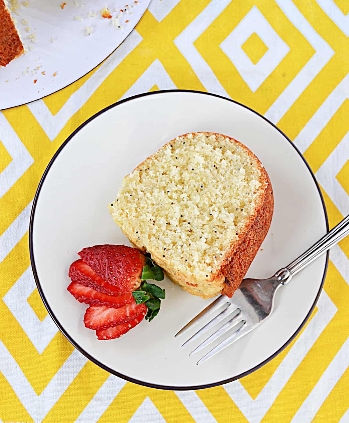 A close up of a slice of lemon Bundt cake on a plate with a strawberry and fork on the plate.