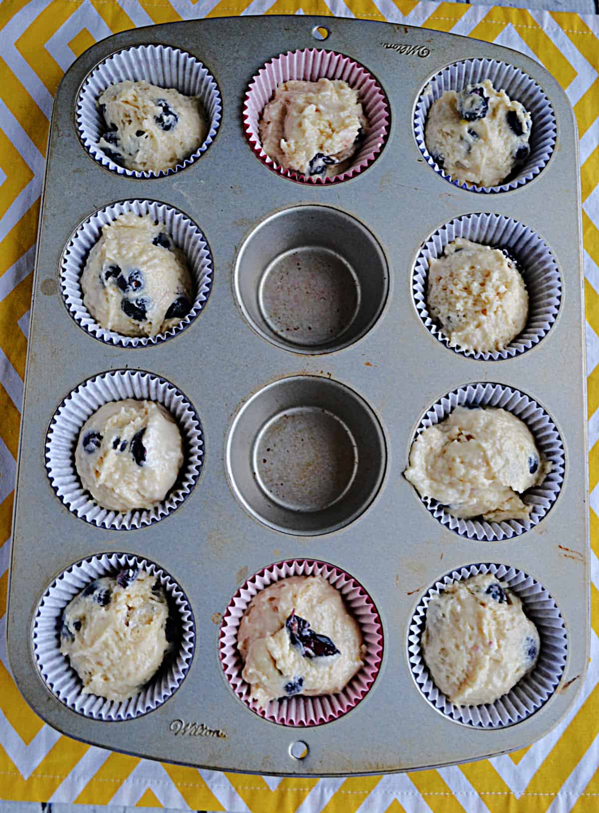 A muffin tin with blueberry muffin dough in it.