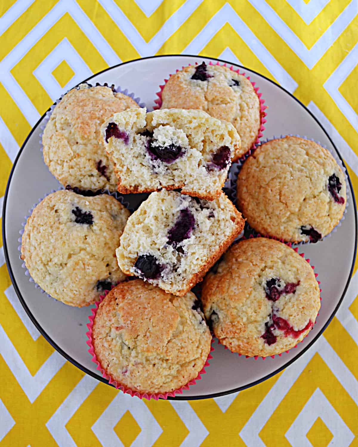 A plate of lemon blueberry muffins with one muffin being cut in half and the inside showing.