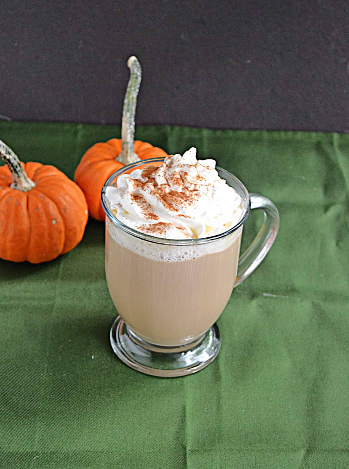 A pumpkin spice latte with two pumpkins behind it.