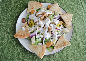 A top view of a plate of salad with chicken and pita bread around the edges.