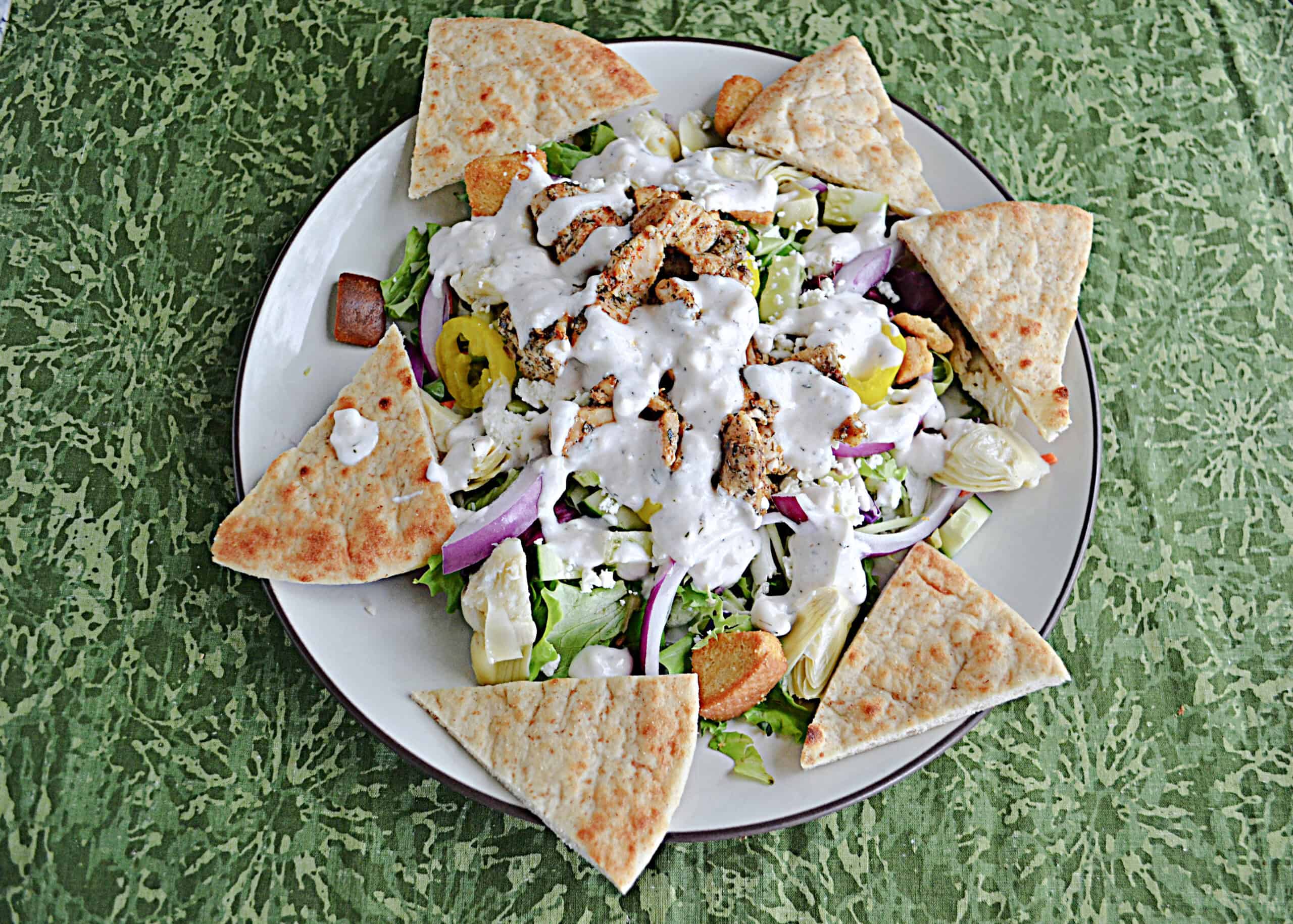 A top view of a plate of salad with chicken and pita bread around the edges.
