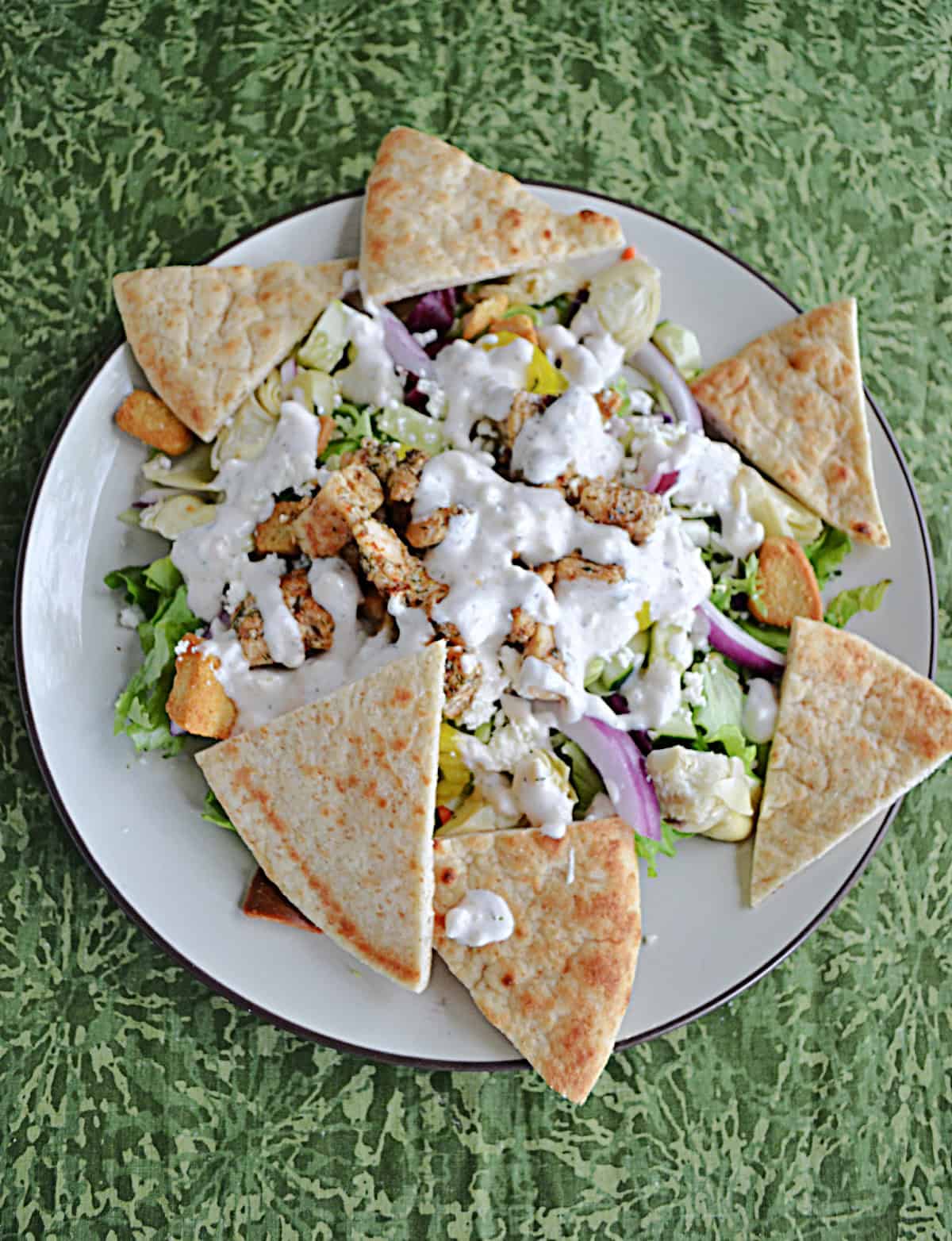 A plate of salad topped with chicken and dressing with pita triangles around the edges.