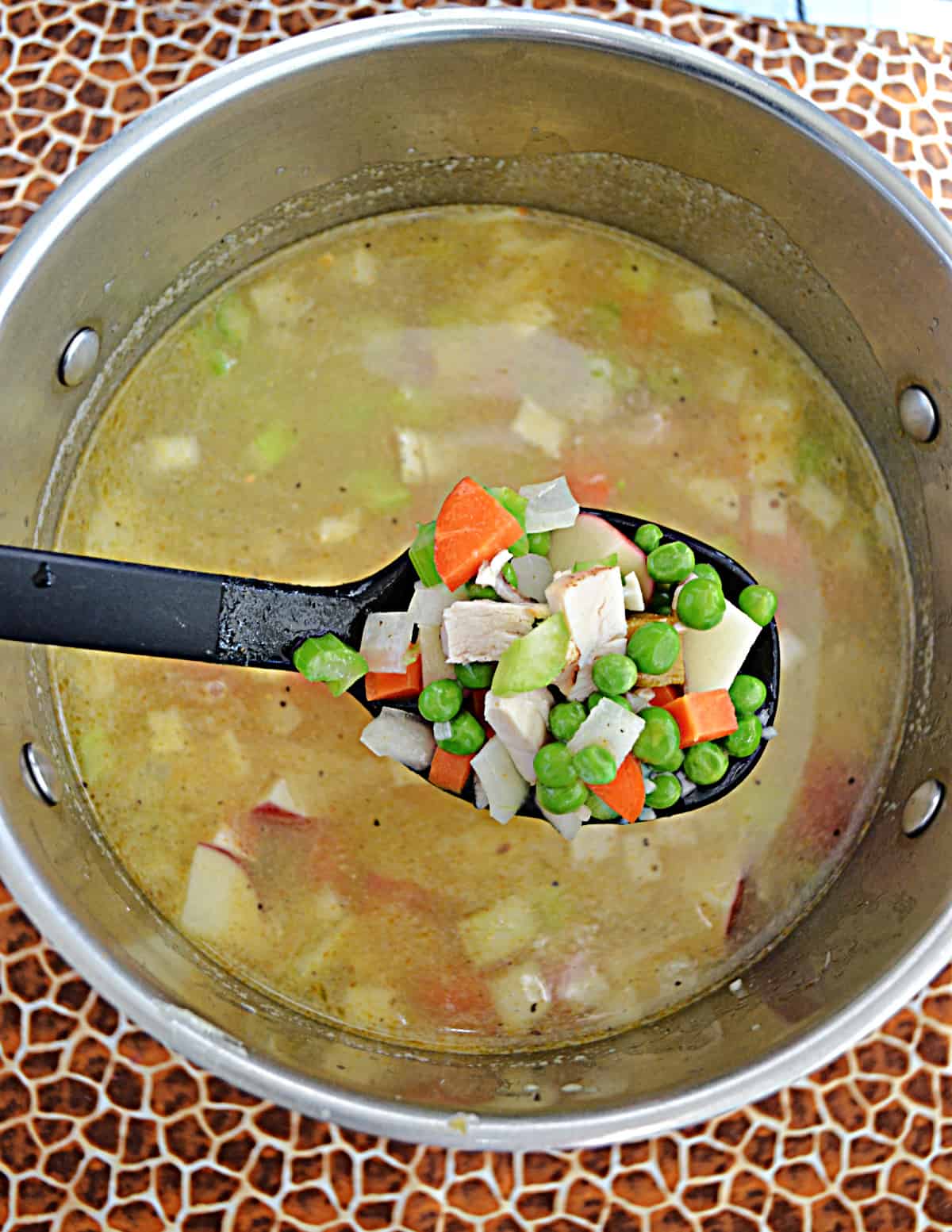 A pot of soup with a spoon holding up a scoop of the vegetables from the soup.