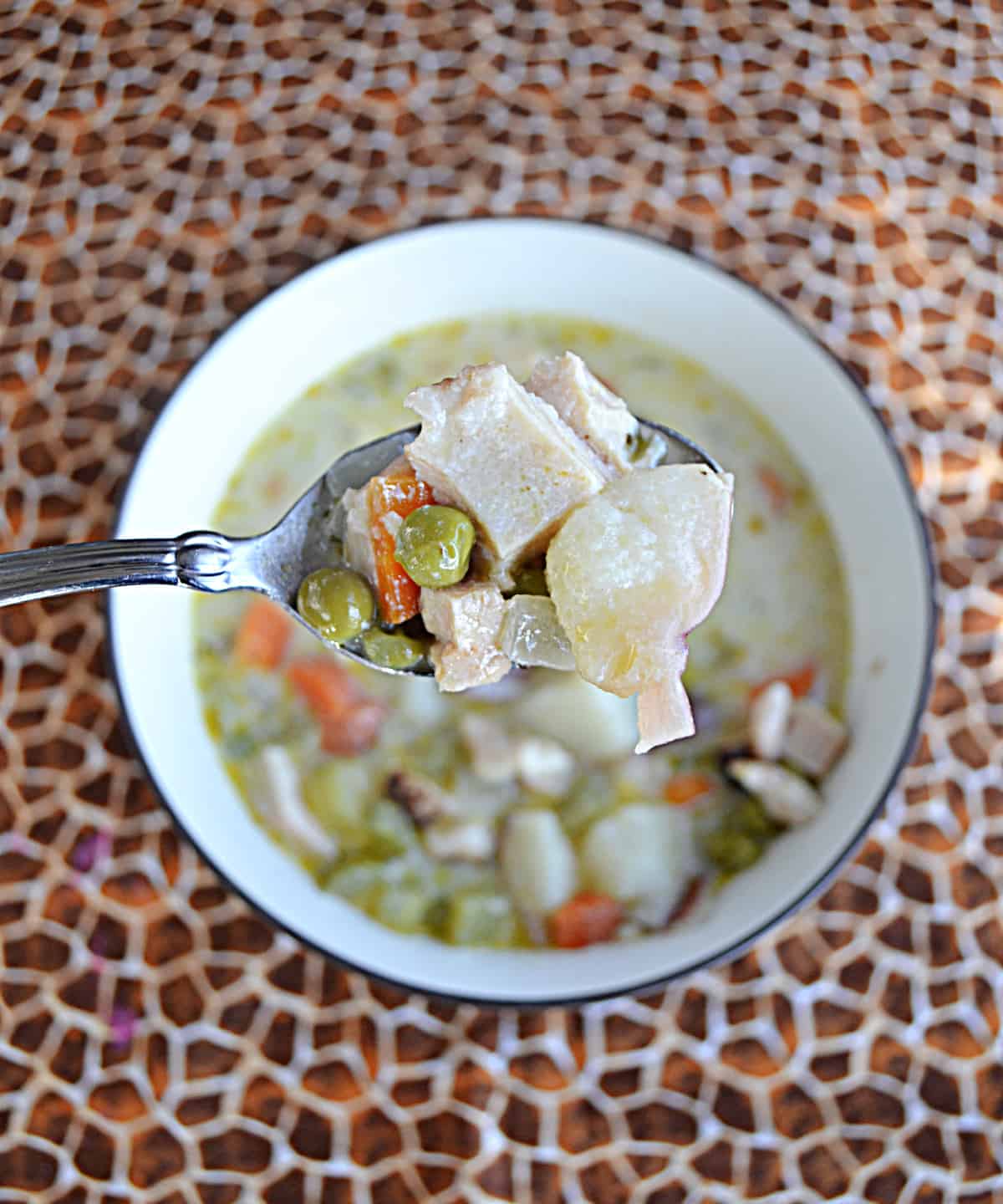 A spoon holding a scoop of the soup with potatoes, chicken, and vegetables on it. 