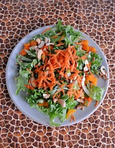 A plate of salad with carrots and cashews on top.