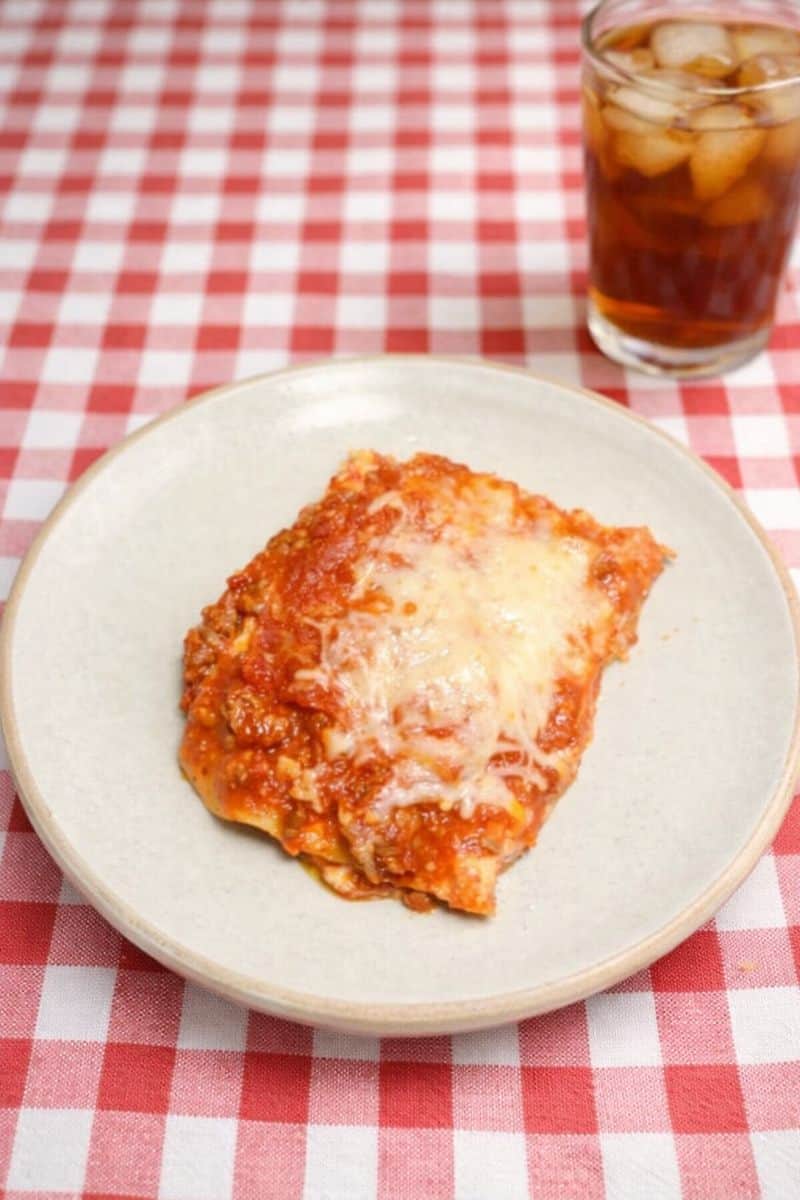 A plate of lasagna with a glass of iced tea in the background.