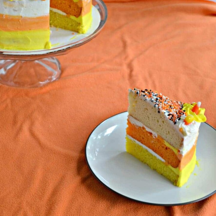 A slice of orange, yellow, and white candy corn cake with the whole cake behind it.